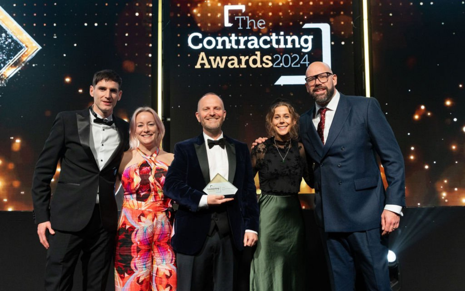 This photo shows 5 people posing on stage for a photo to celebrate VIQU winning 'Best Contractor Recruitment Agency'